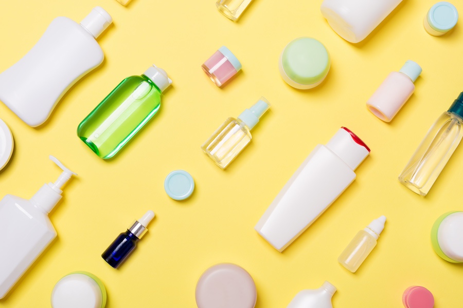 A range of cosmetic and beauty products produced by a contract manufacturing organization are arrayed across a yellow background.